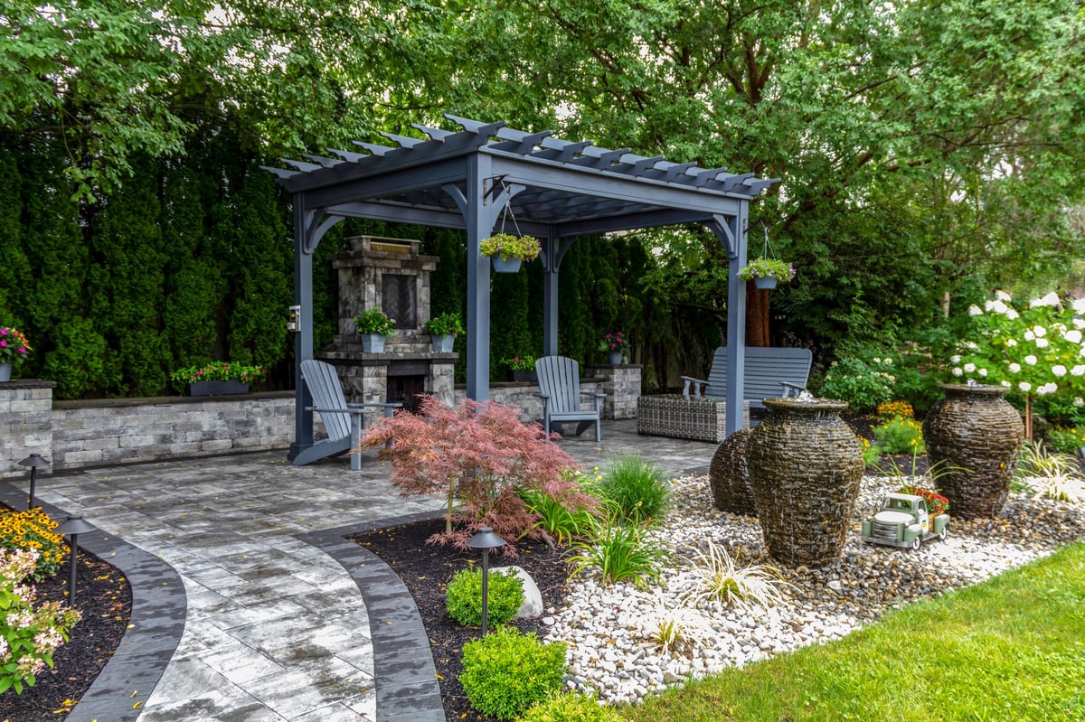 Large gray pergola on pavers with stone fireplace and waterfall urns